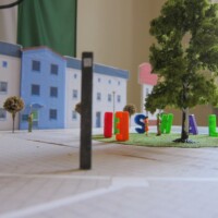 Modell mit grüner Insel, dichtem Baum, bunte 3D-Buchstaben ringsum, Figuren und Häuser im Hintergrund