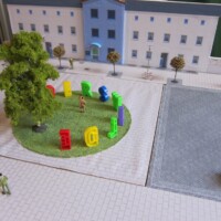 Stadtmodell mit Gebäuden, großem Baum und farbigen Buchstaben auf grünem Platz