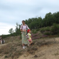 Frau mit Kind auf Sandschliff mit Vegetationsrand und Waldkulisse im Hintergrund