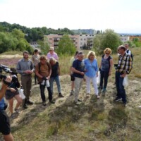 Exkursionsgruppe auf Trockenrasen mit Film-Dokumentation, Siedlungshintergrund