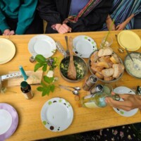 Essenstisch mit Tellern, Besteck, serviertem Essen und frischen Kräutern als Dekoration.