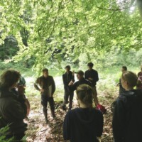 Exkursionsgruppe steht im Laubwald unter dichtem Blätterdach