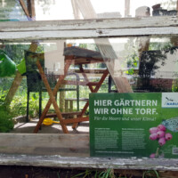 Ein Schild "Hier gärtnern wir ohne Torf" am Gewächshaus