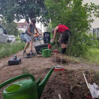 Zwei Menschen gießen Beton in Plastikröhren, die im Boden eingegraben sind
